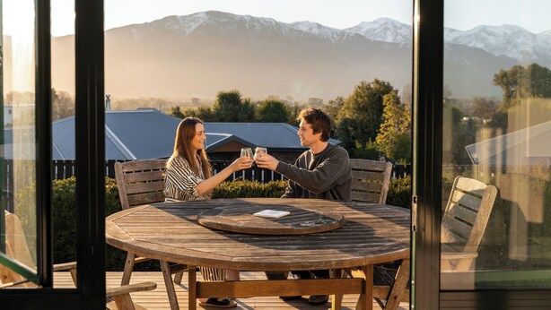 A couple sitting at a wooden table with a view of snow-capped mountains in the background. - Handy to Town | Spacious | Relaxed - KK14905 (Kaikoura)