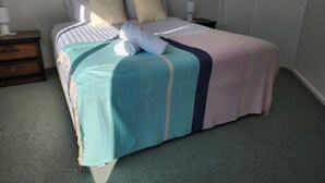 A neatly made bed with a striped pillowcase, a teal and pink bedspread, and two white towels. - Handy to Town | Spacious | Relaxed - KK14905 (Kaikoura)