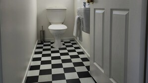 A narrow hallway with a black and white checkered floor, a white toilet, and a door with a mirror. - Handy to Town | Spacious | Relaxed - KK14905 (Kaikoura)