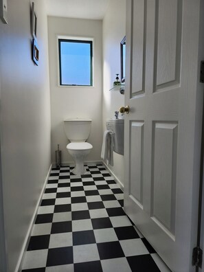 Un pasillo estrecho con piso a cuadros blanco y negro, un inodoro blanco y una puerta con espejo.