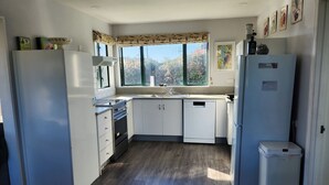 A compact kitchen with white cabinets, a built-in oven, a microwave, a sink, and a refrigerator. - Handy to Town | Spacious | Relaxed - KK14905 (Kaikoura)