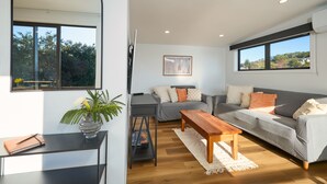 Uma sala de estar moderna com um sofá cinzento, mesa de centro de madeira e um suporte preto para televisão.