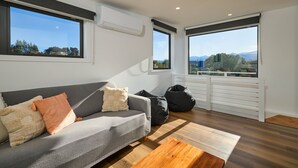 Sala de estar moderna com um sofá cinza, uma mesa de centro de madeira e vista para o exterior através de grandes janelas.