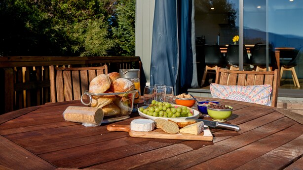 Uma mesa de madeira com diversos alimentos, incluindo pão, queijo, uvas e uma tigela de nozes.