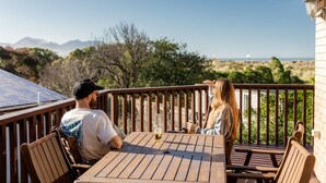 Eine Holzterrasse mit Tisch und Stühlen, mit Blick auf eine Landschaft mit Bergen und Vegetation.