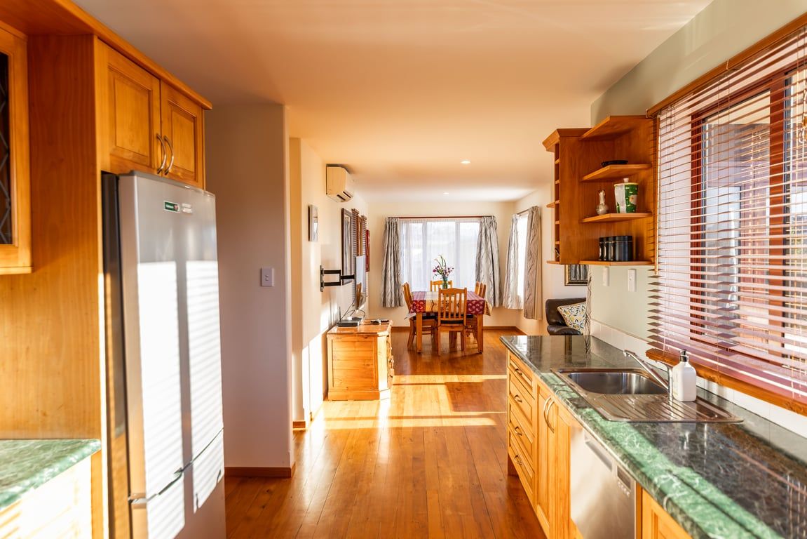 Una cocina con armarios de madera, un refrigerador de acero inoxidable, una mesa de comedor con sillas y un ventanal con persianas.
