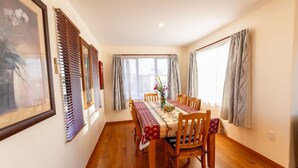 A dining area with a wooden table, chairs, and a vase of flowers. - Coastal | Spacious | Mountain Views - KK21238 (Kaikoura)