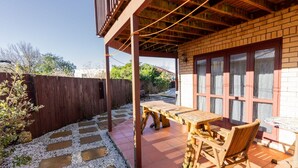 Eine Terrasse im Freien mit einem Holztisch und -stühlen, einer Ziegelwand und einem Holzzaun.