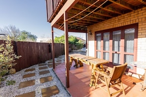 Une terrasse extérieure avec une table et des chaises en bois, un mur en briques et une clôture en bois.