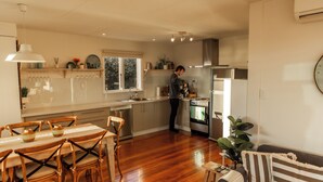 Una cocina moderna con suelo de madera, un comedor con mesa y sillas, y una sala de estar con sofá y un reloj en la pared.