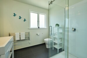 Un bagno moderno con box doccia in vetro, un water bianco, porta doccia in vetro e una finestra decorata con tre farfalle blu.