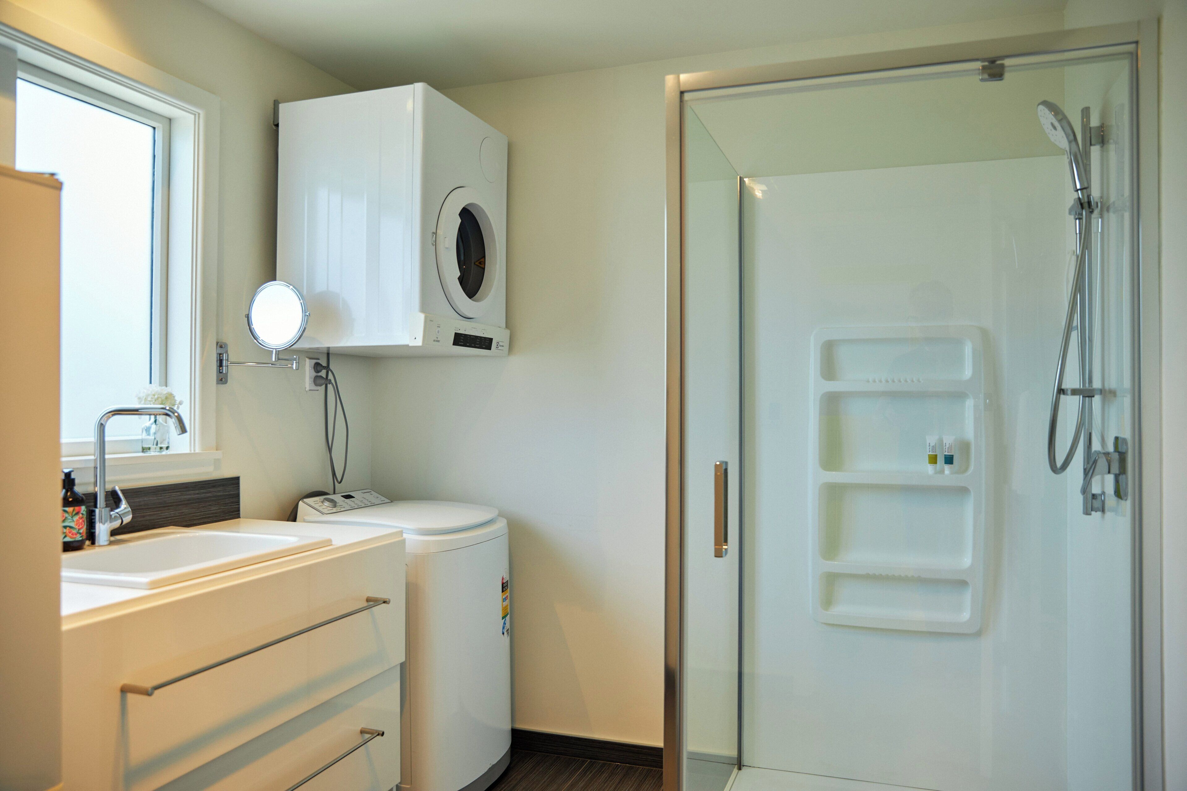 Un baño moderno con lavadora integrada, un lavamanos con espejo y zona de ducha con estantes.