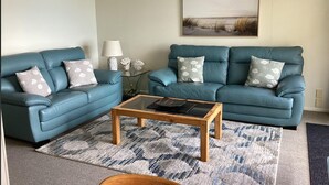 A living room with two blue sofas, a wooden coffee table, and a patterned rug. - Spectacular Views | Convenient | Affordable - KK17129 (Kaikoura)