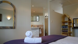 A bedroom with a bed, a bathroom with a sink, and a mirror. - Spectacular Views | Convenient | Affordable - KK17129 (Kaikoura)
