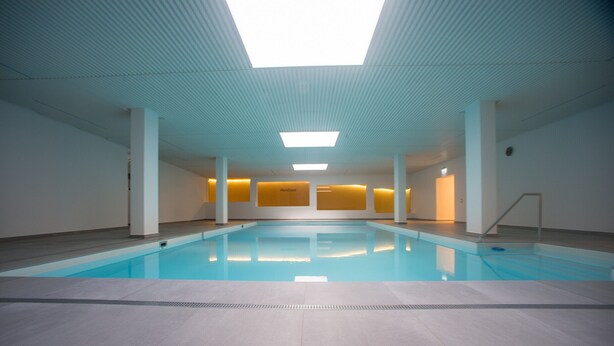 Una piscina con techo de tragaluces, paredes blancas y suelo de baldosas.