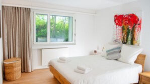 Un dormitorio con cama, ventana, mesita de noche y una obra de arte colgada en la pared.