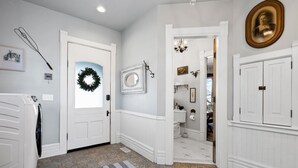 A hallway with a white door, a wreath, a mirror, and a chandelier.