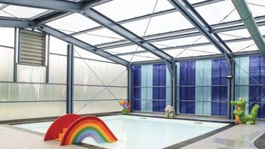 An indoor swimming pool with a glass ceiling, a rainbow play structure, and a crocodile statue. - Mooie rustige woning Overijssel. (Gramsbergen)