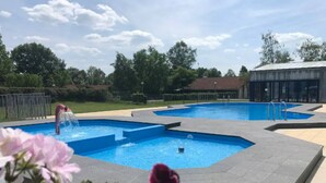 A swimming pool with a unique geometric design, surrounded by a fence and a building in the background. - Mooie rustige woning Overijssel. (Gramsbergen)