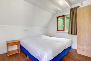 A bedroom with a single bed, a wooden nightstand, a window with curtains, and a wardrobe.