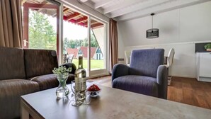Een woonkamer met een bank, fauteuil en een tafel met een fles en bloemen.
