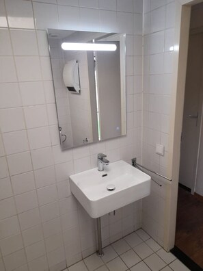 Een badkamer met een witte wastafel, een spiegel en een handdroger.