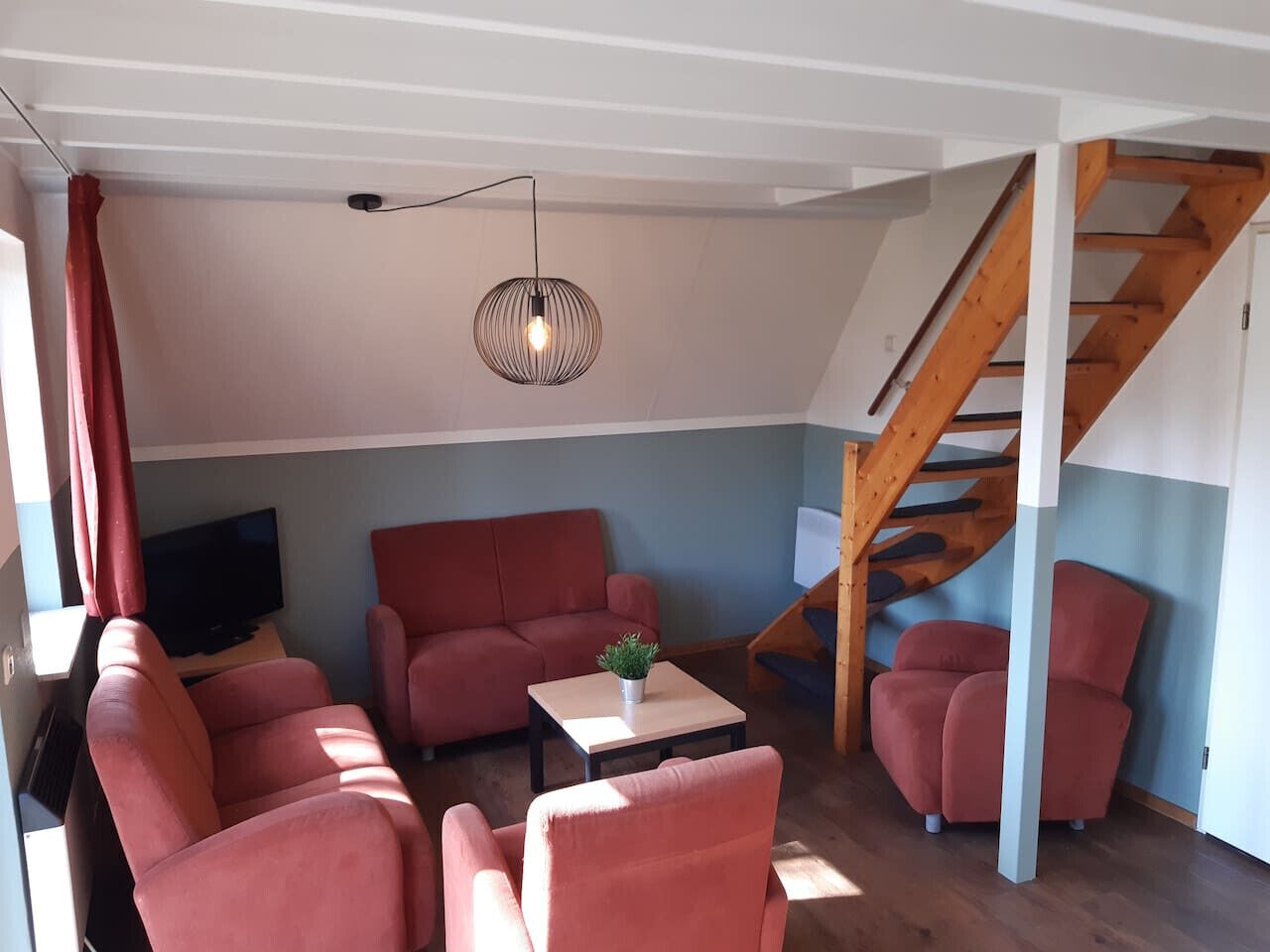 A living room with a red sofa set, a coffee table with a plant, a TV, and a wooden staircase.
