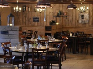 A restaurant with wooden walls and chandeliers, tables set with wine glasses and plates, and a sign indicating a special menu. - Leuke gezinswoning op park (Gramsbergen)