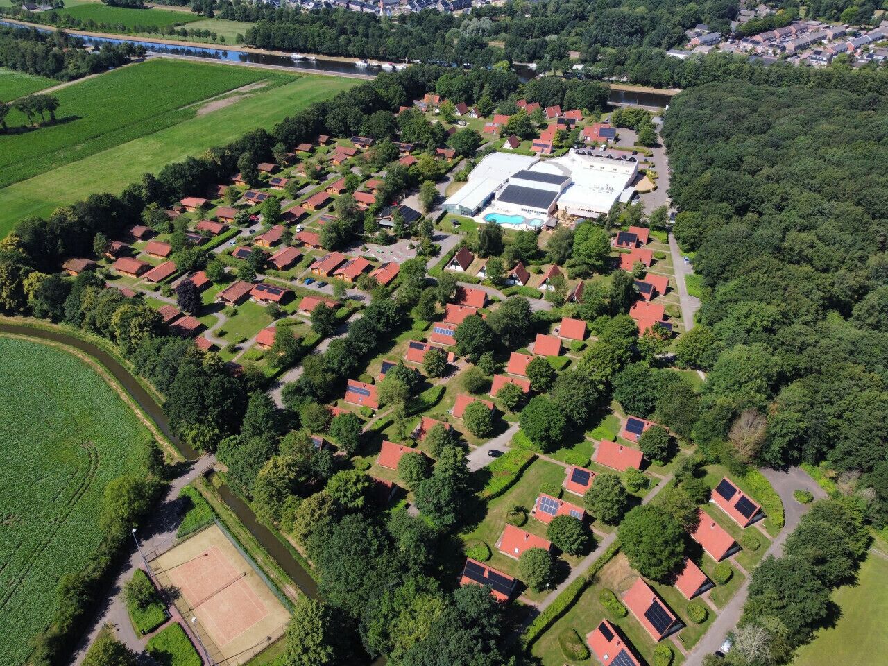 Oversigtsbillede af et boligområde med huse, en stor bygning med swimmingpool og grøn vegetation omkring.