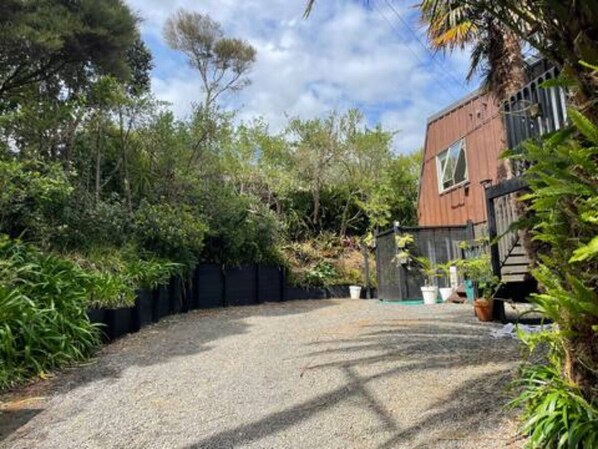 A gravel driveway leading to a wooden house with a fenced backyard.
