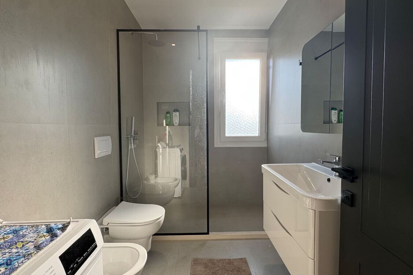 A modern bathroom with a glass-enclosed shower, a toilet, and a sink.