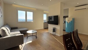 Ein modernes Wohnzimmer mit einer Couch, einem kleinen runden Tisch, einem Flachbildfernseher und einem blauen Kühlschrank.