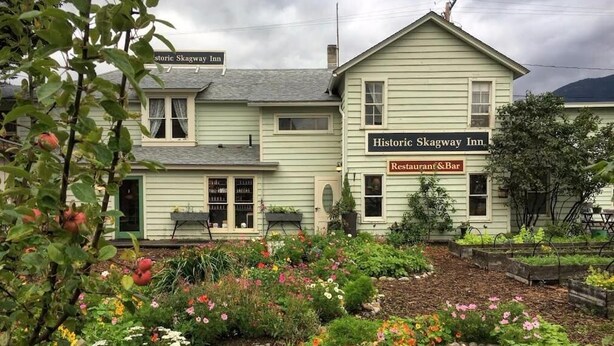 Ein historisches Gebäude mit einem Schild für das Skagway Inn, mit einem Garten mit verschiedenen Pflanzen und Blumen.
