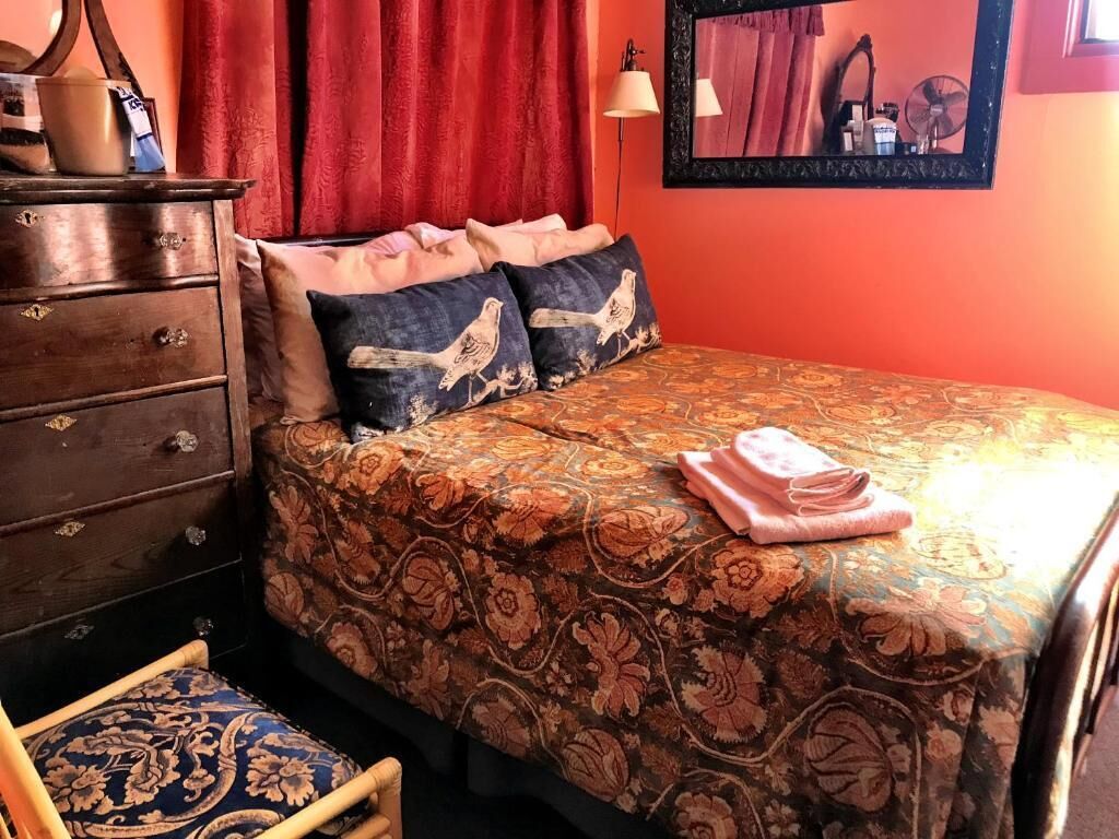 Un dormitorio con cama, almohadas, cómoda, una silla y un espejo en la pared.