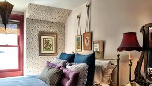 Ein Schlafzimmer mit Bett, Kissen, Kommode, Lampe, Spiegel und Wandbildern.
