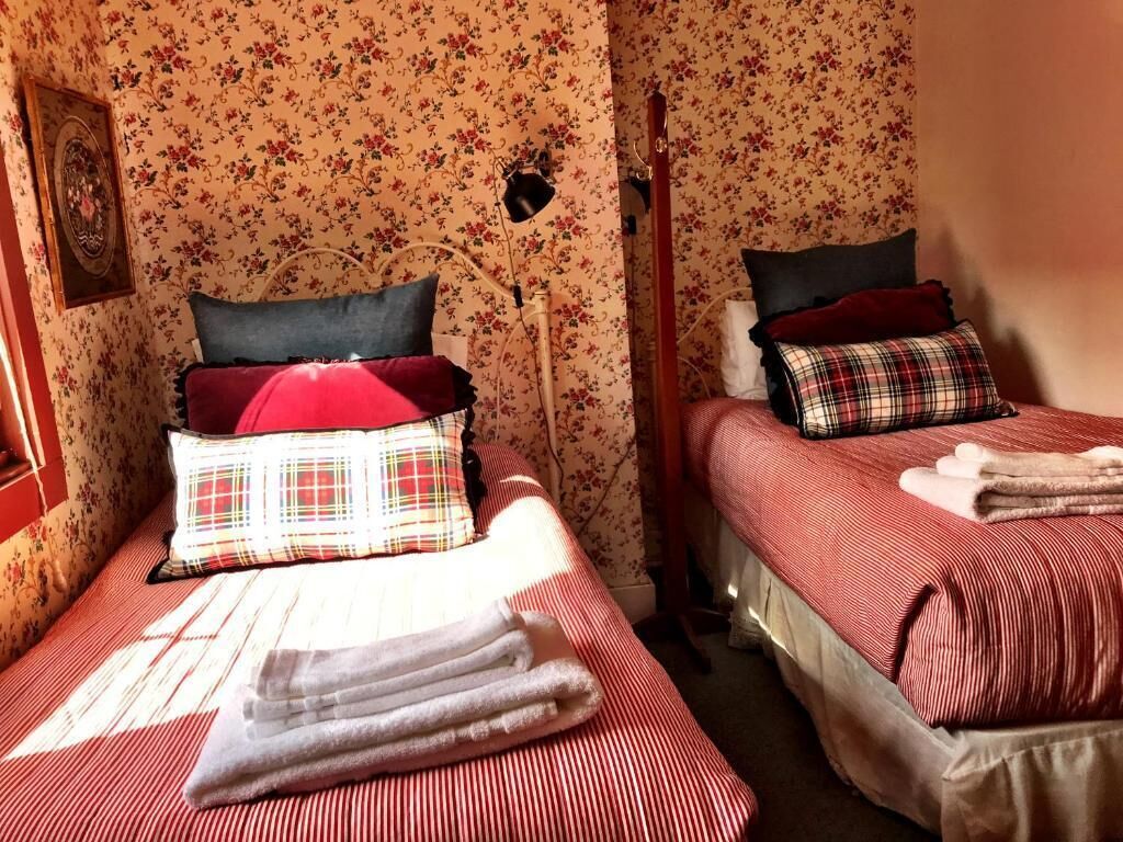 Een kamer met twee bedden, bloemenbehang, een lijst met een foto en een bedlamp.
