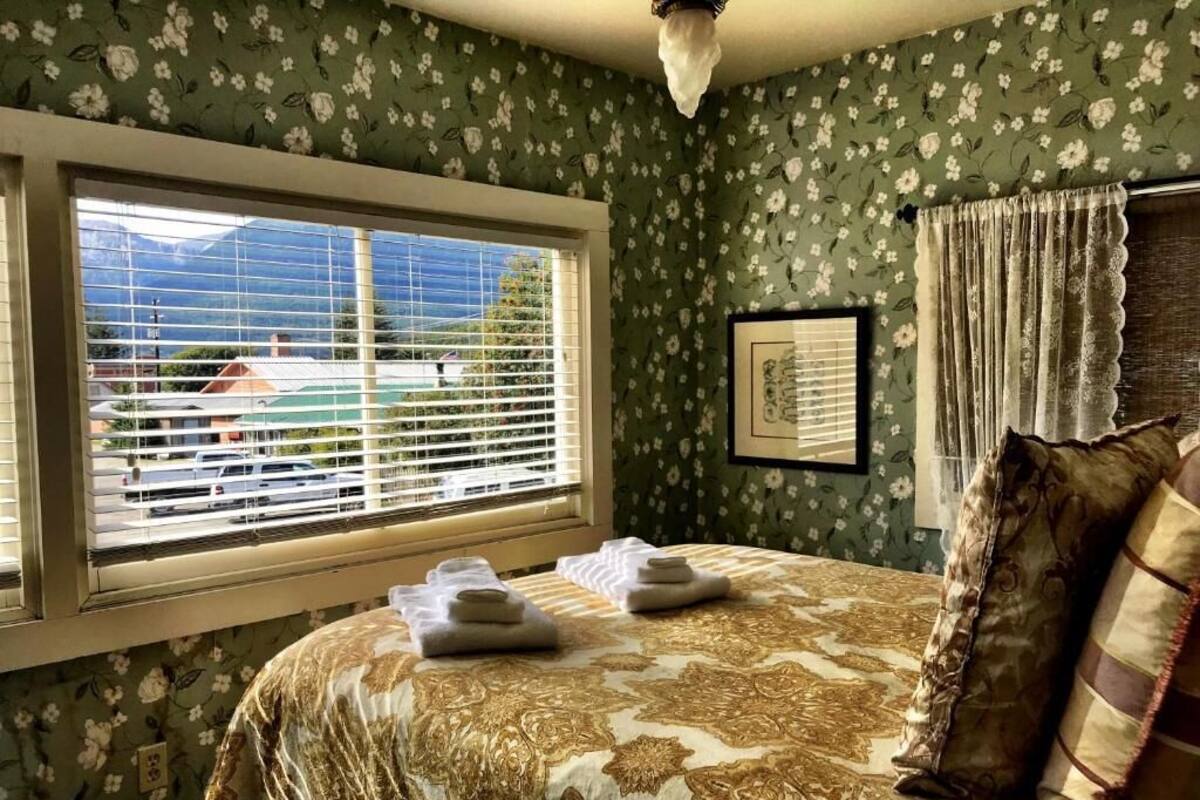 A bedroom with a bed, a window with blinds, a framed picture on the wall, and a curtain.