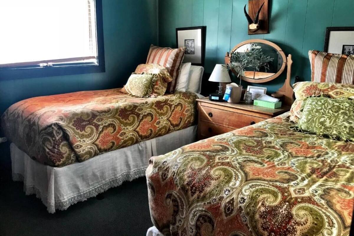 A room with two beds, a dresser, a mirror, and a window.