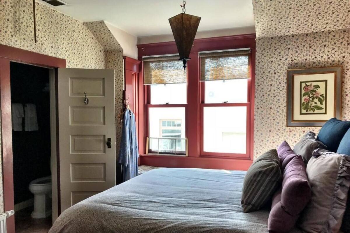 A bedroom with a bed, a door, a window, and a framed picture on the wall.