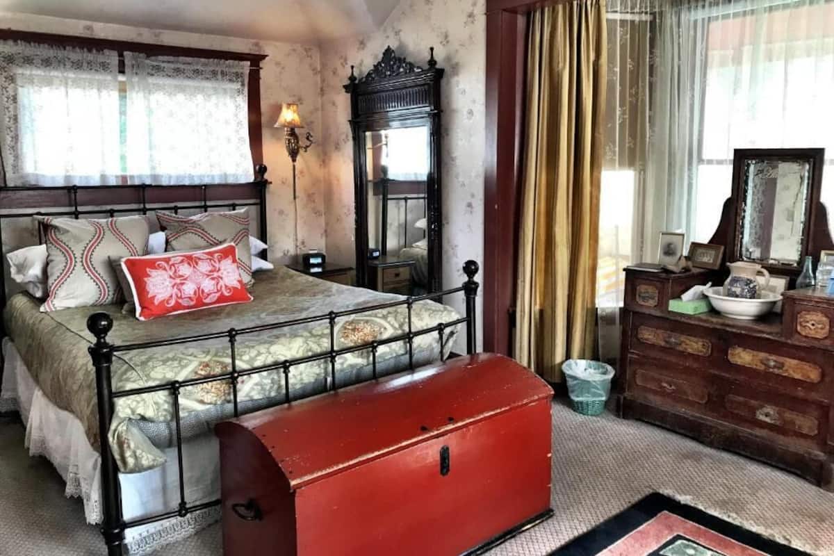 A bedroom with a bed, a dresser, a mirror, and a window with curtains.