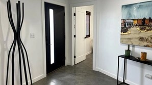 A hallway with a black door, a painting on the wall, and a small table with a plant and a can.