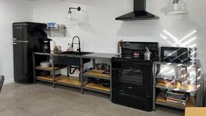 A modern kitchen with a black refrigerator, stove, and microwave. There is a sink with a faucet, and a shelf with kitchen items.