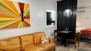 Ein Zimmer mit einer Ledersofa, einem Esstisch mit Stühlen, einer Wandklimaanlage und einem farbenfrohen abstrakten Gemälde.