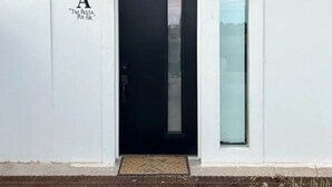 Ein modernes Gebäude mit einer schwarzen Tür, einem kleinen Fenster und einem Buchstaben ‚A‘ als Zimmernummer.