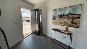Un couloir avec une porte-fenêtre coulissante donnant sur un espace extérieur, une console noire ornée de livres et d’une boîte, et un grand tableau représentant un paysage accroché au mur.