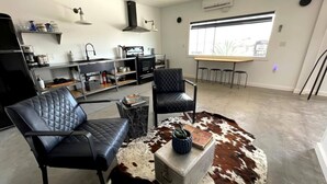 Un salon moderne avec des fauteuils en cuir, un tapis en peau de vache et un coin cuisine comprenant une table à manger.
