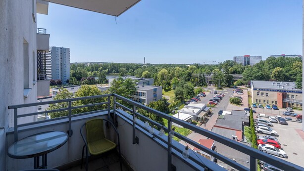 Un balcon avec une chaise et une table, donnant sur un parking et des immeubles, avec de la verdure en arrière-plan.