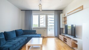 Un salon moderne avec un canapé bleu, une table basse blanche et un téléviseur posé sur un meuble en bois.