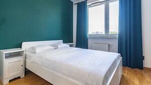 Une chambre à coucher avec un lit, des tables de chevet, une fenêtre avec des rideaux et une vue sur les bâtiments à l’extérieur.