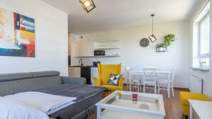 A modern living room with a grey sofa, a yellow armchair, and a white coffee table. There is a kitchen in the background with white cabinets and a microwave. - Urban Chic Apartment (Katowice)